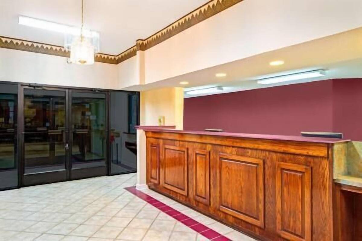 A hotel lobby with a reception desk, a glass door entrance, and a tiled floor.