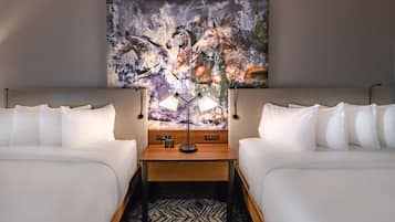 Habitación de hotel con dos camas, una mesita de noche de madera, una lámpara moderna y un cuadro abstracto grande en la pared.