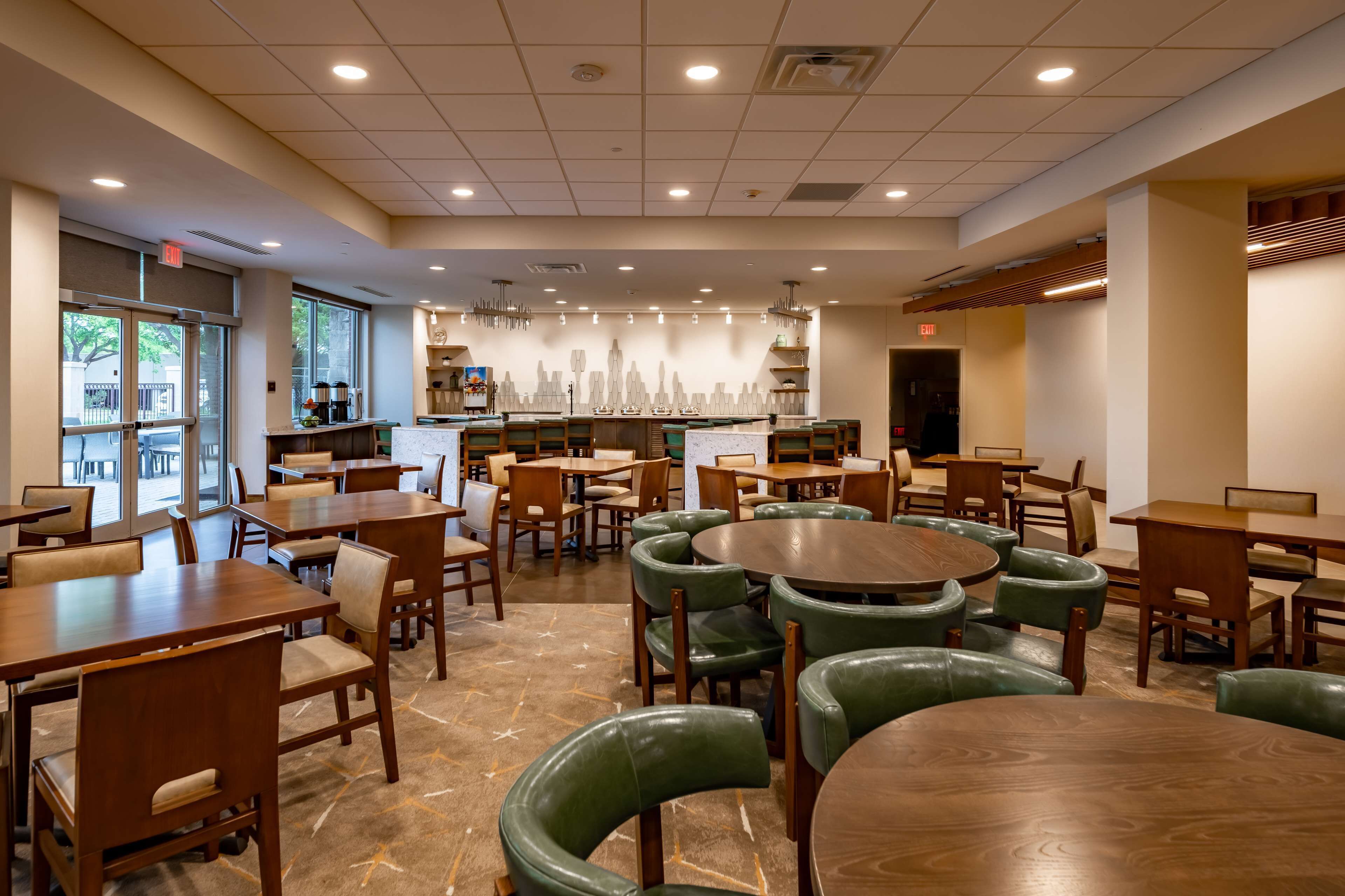 Un restaurant spacieux, doté de nombreuses tables et chaises, d’un bar central et de grandes fenêtres laissant entrer la lumière naturelle.