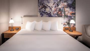 A neatly made bed with white linens, two bedside tables with lamps, and a large abstract painting on the wall.