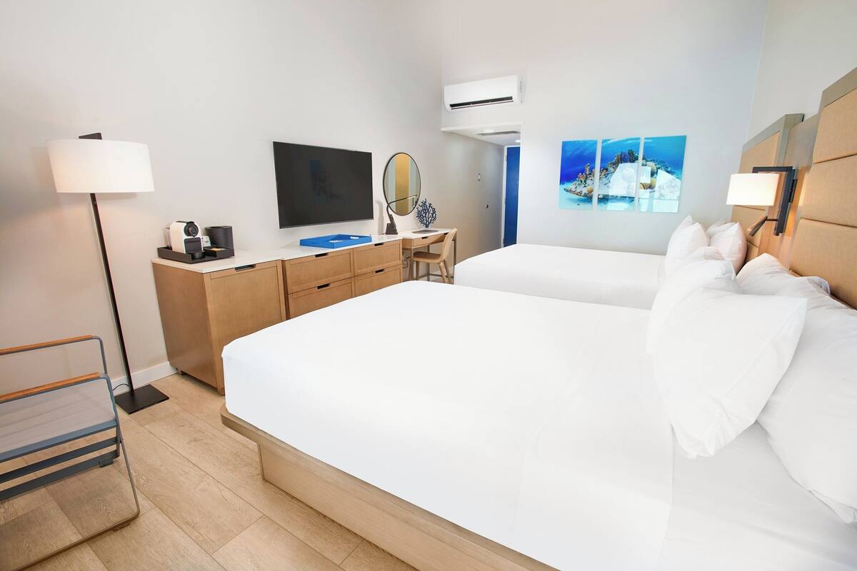 Habitación de hotel con cama, escritorio, silla, televisión, espejo y cuadros en la pared.