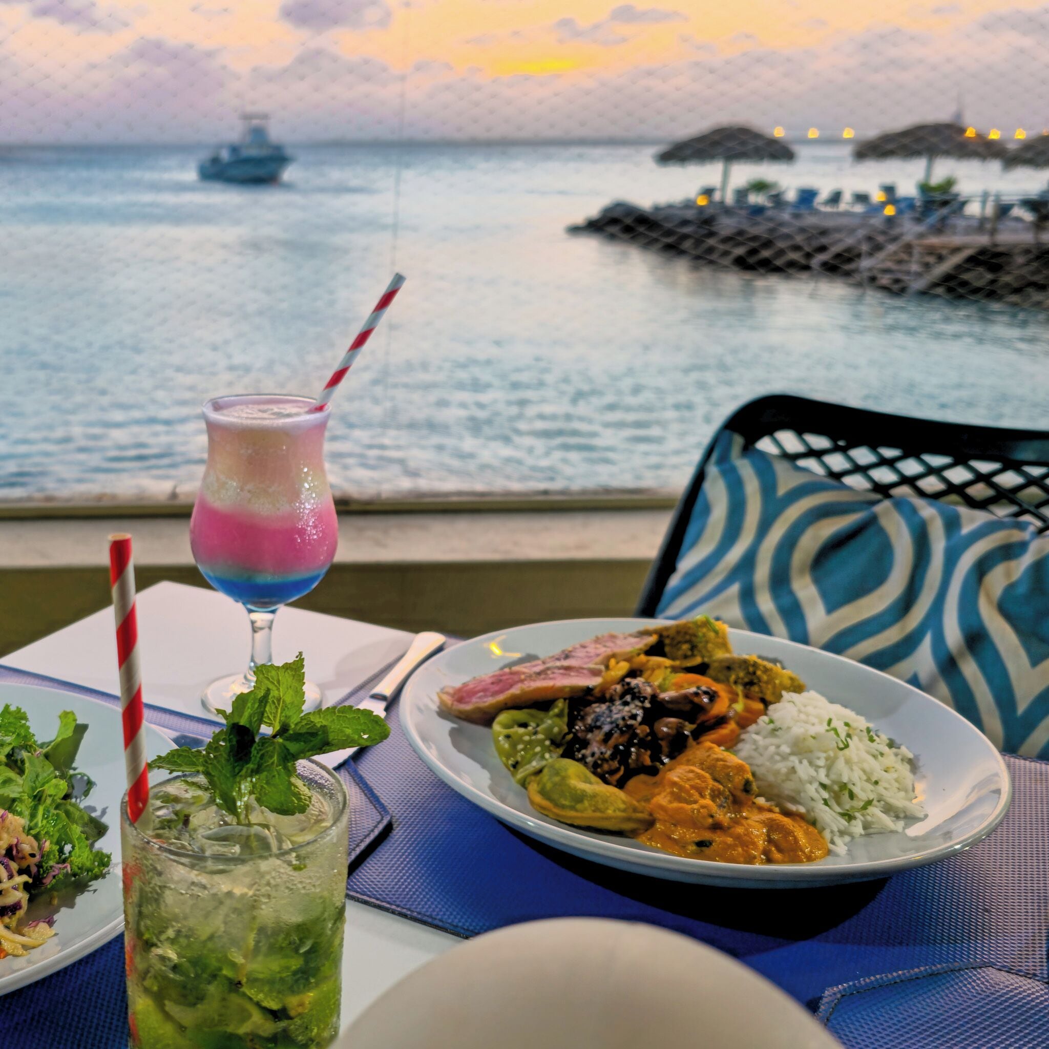 Un repas composé de différents plats et boissons, servi sur une table avec vue sur le bord de l’eau.