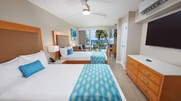 Quarto de hotel com duas camas, televisão, escrivaninha e varanda com vista para o oceano.