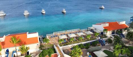 A resort with a pool, lounge chairs, and a view of the ocean with boats.