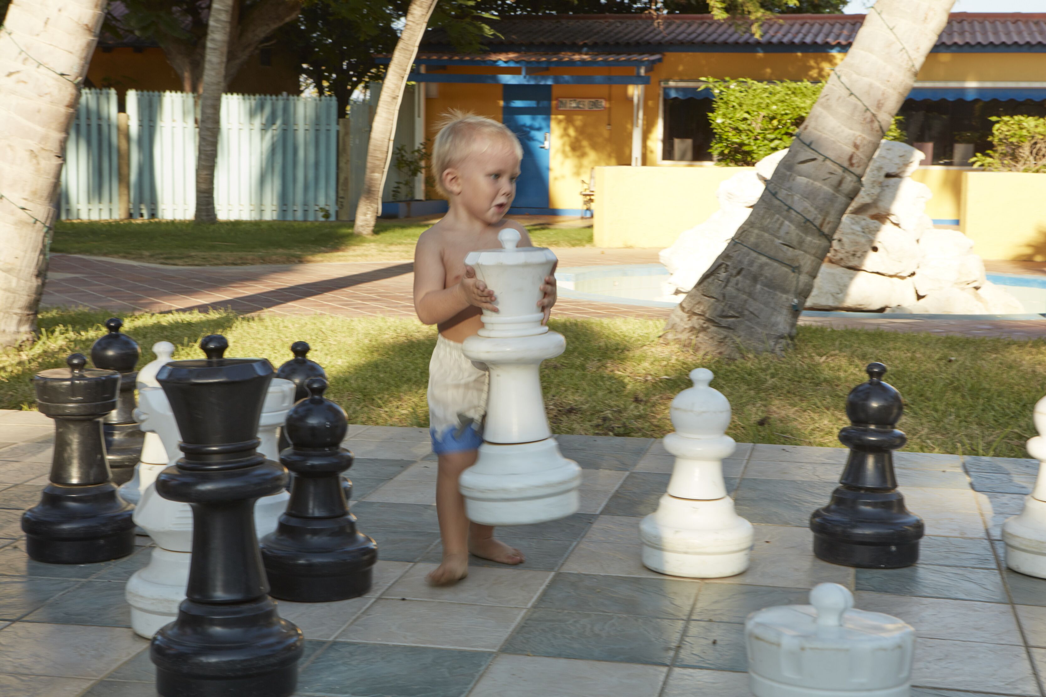 A child playing chess on a tiled outdoor area with large chess pieces.