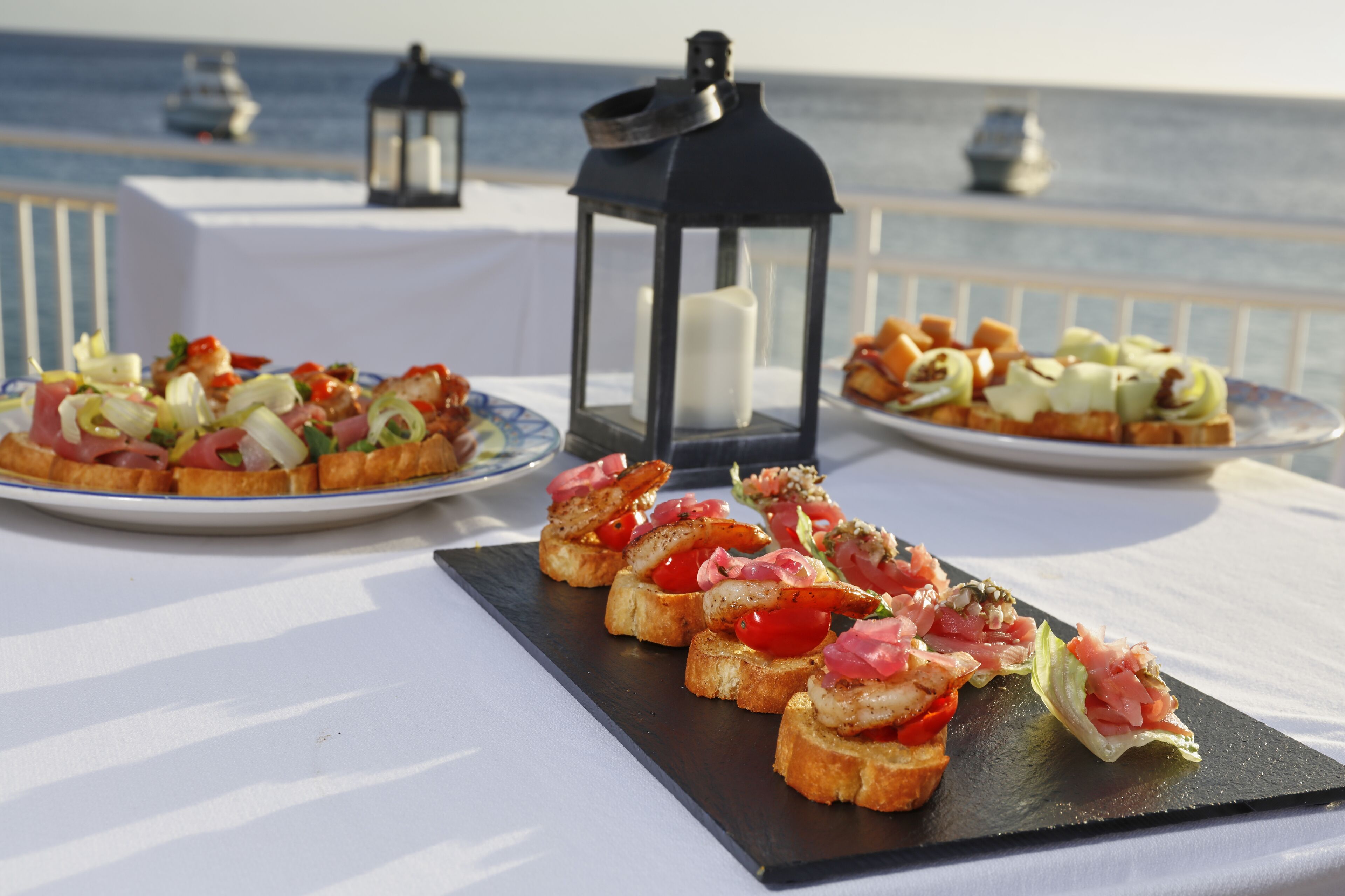 A table with various appetizers and a lantern, set against a view of the sea.