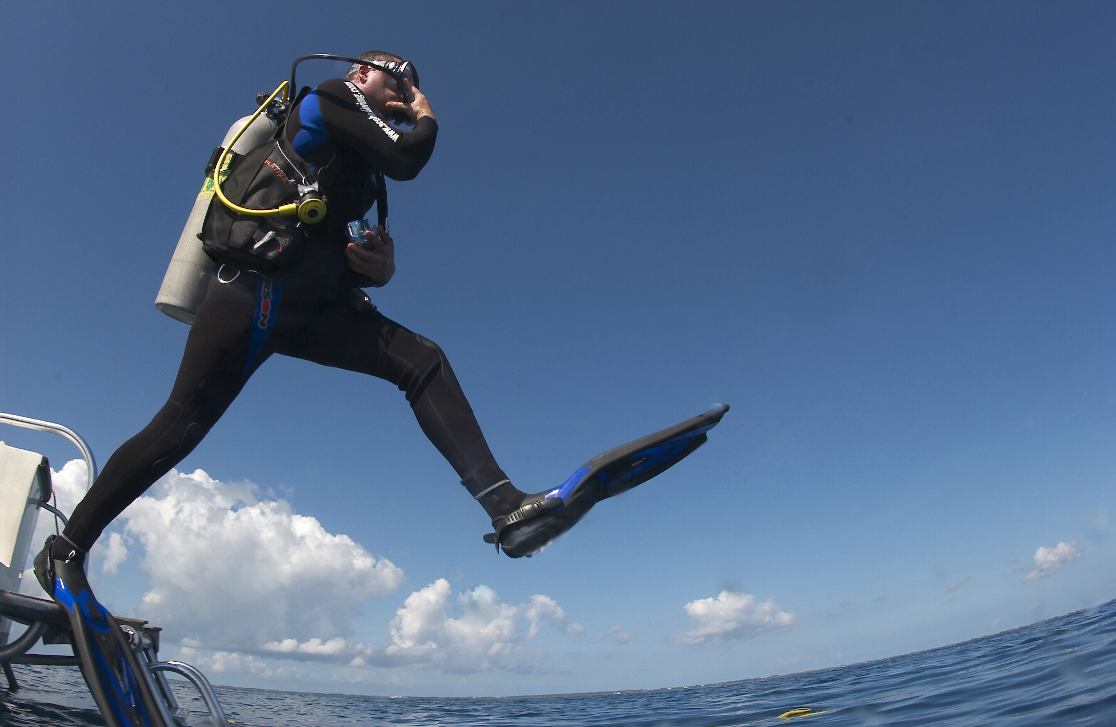 A diver in a wetsuit and fins, preparing to jump into the water.