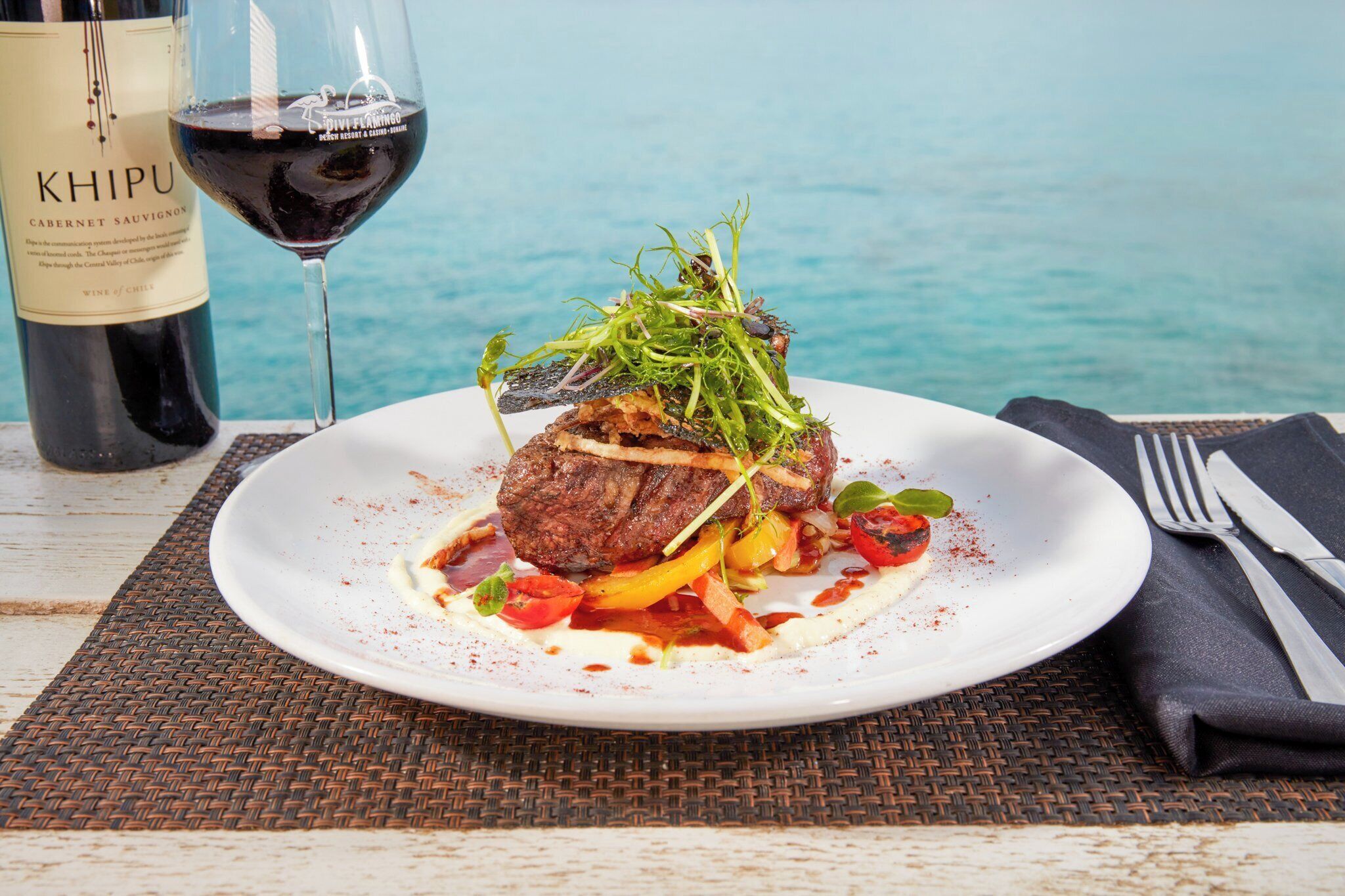 Ein Teller Essen mit einer Weinflasche und Blick aufs Meer.