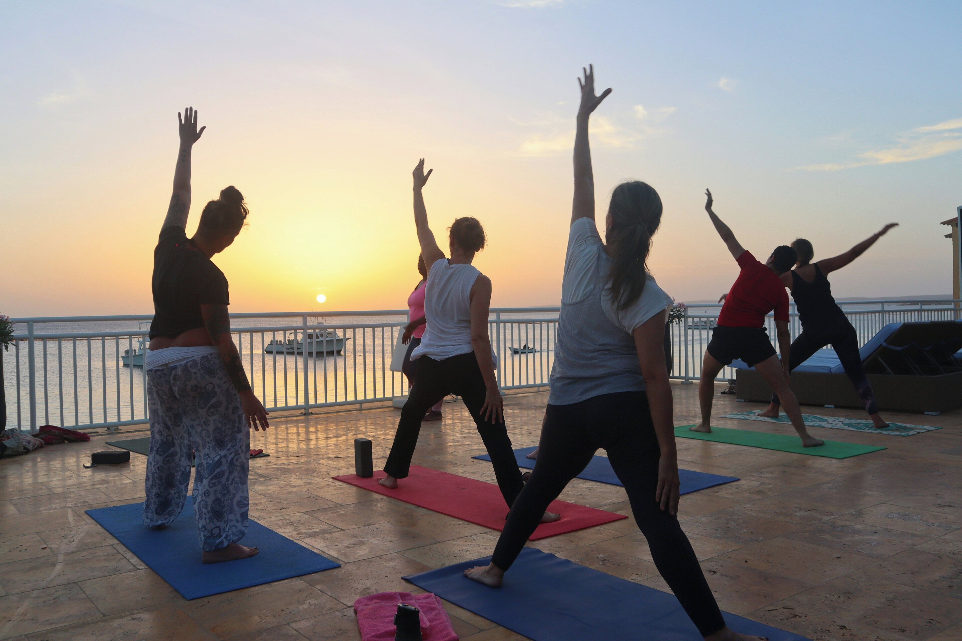 Un gruppo di persone pratica yoga su tappetini, con vista sul tramonto.