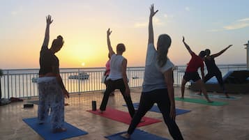 Un gruppo di persone pratica yoga su tappetini, con vista sul tramonto.