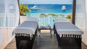 Een balkon met twee massagetafels, uitzicht op zee en boten.