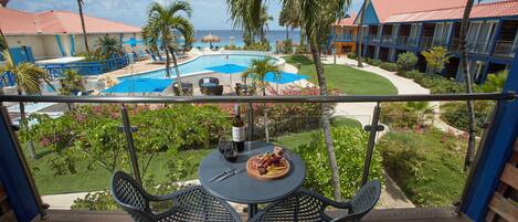 A balcony with a table set for two, overlooking a swimming pool and a resort building.