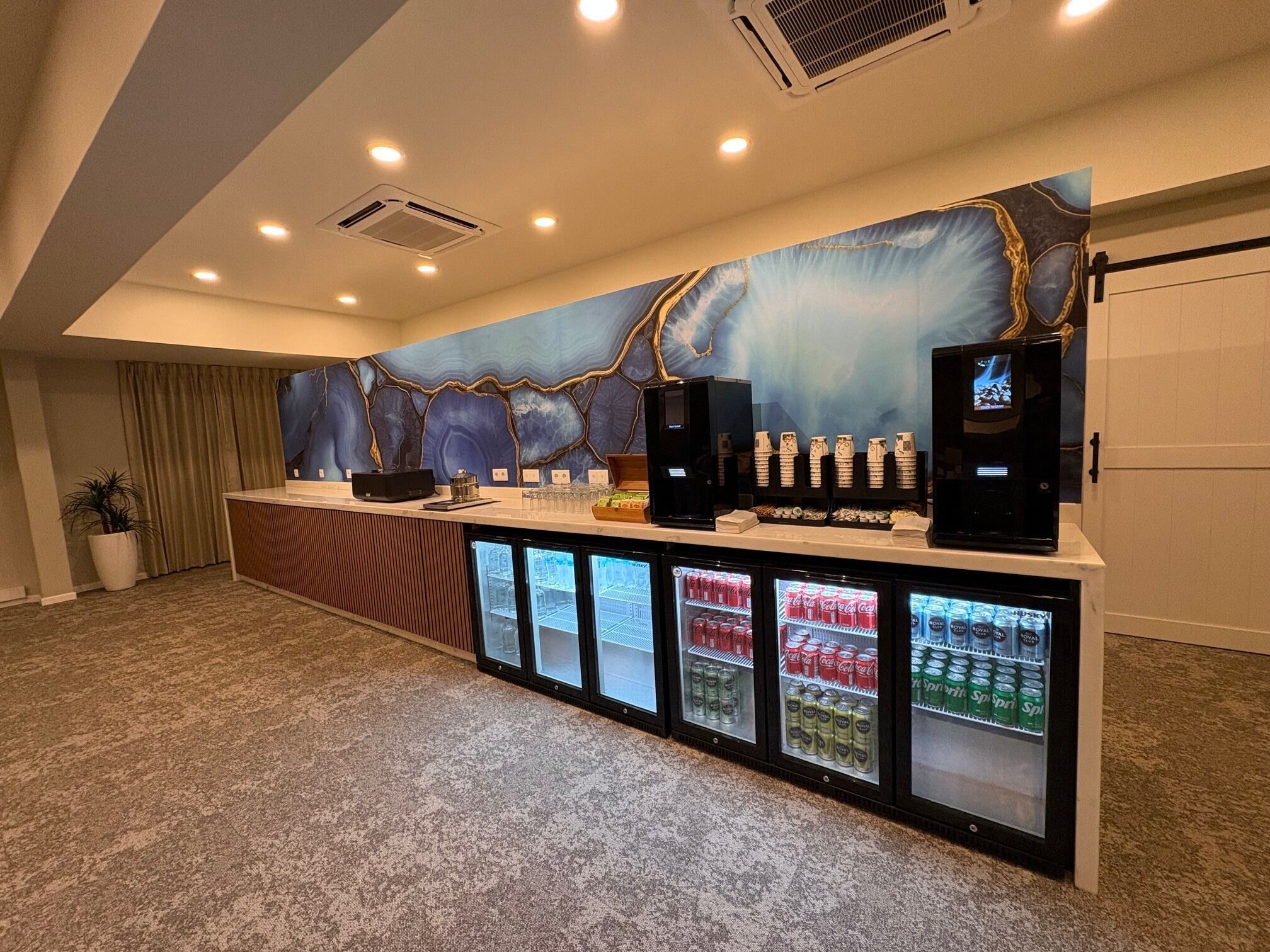 Un área de recepción con mostrador de mármol, dispensadores de bebidas y un mural grande en la pared.
