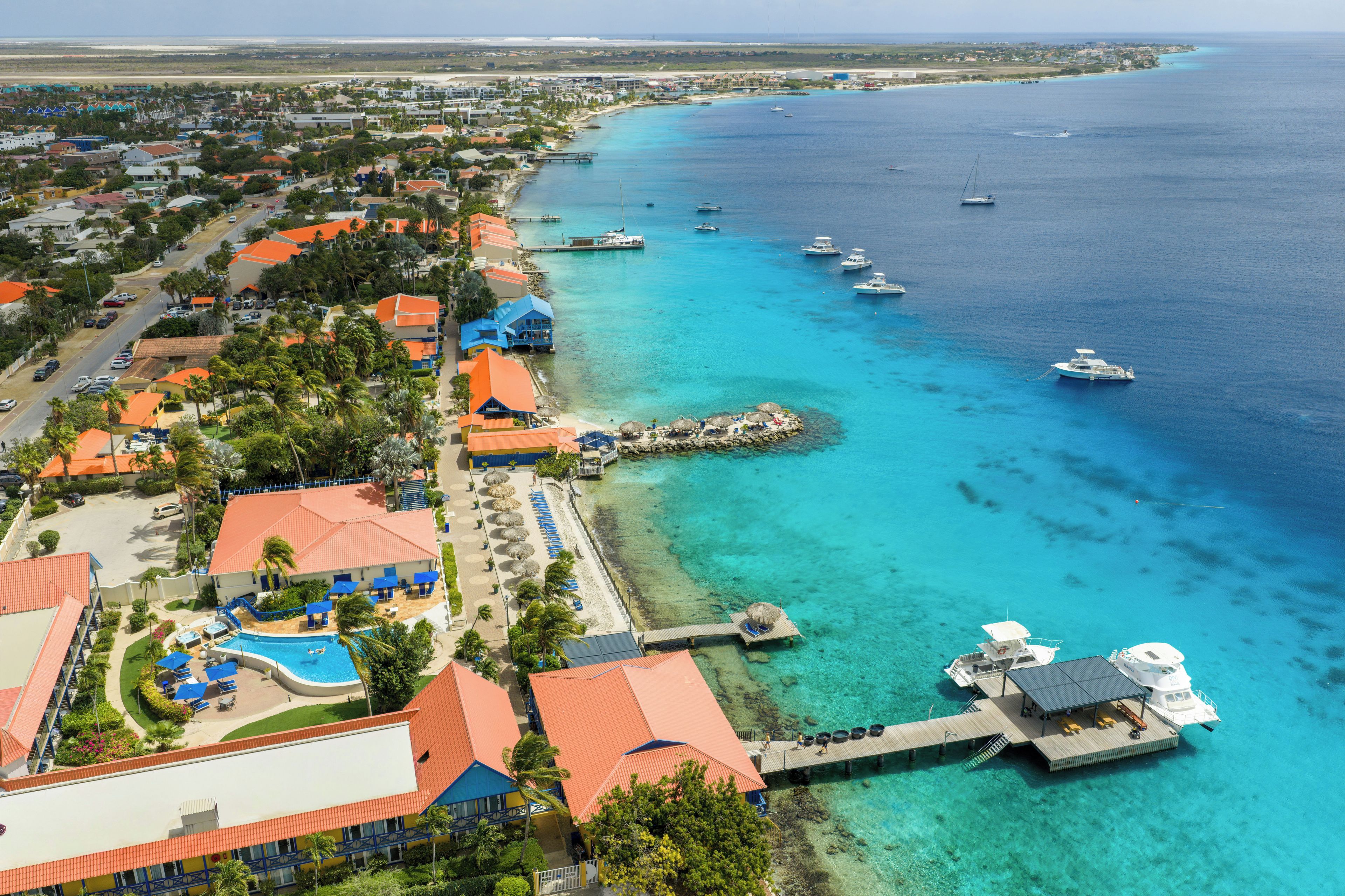 A coastal resort with a pier, clear turquoise waters, and a variety of buildings with red roofs.
