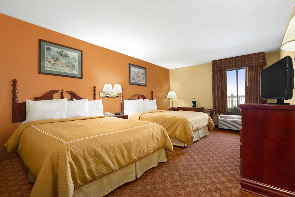 A hotel room with two beds, a television, and a window with curtains.