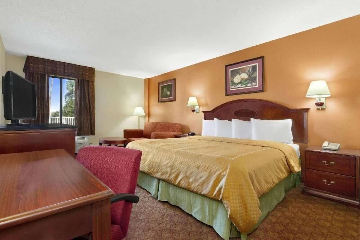 A hotel room with a bed, a desk, a chair, a TV, and two wall-mounted lamps.