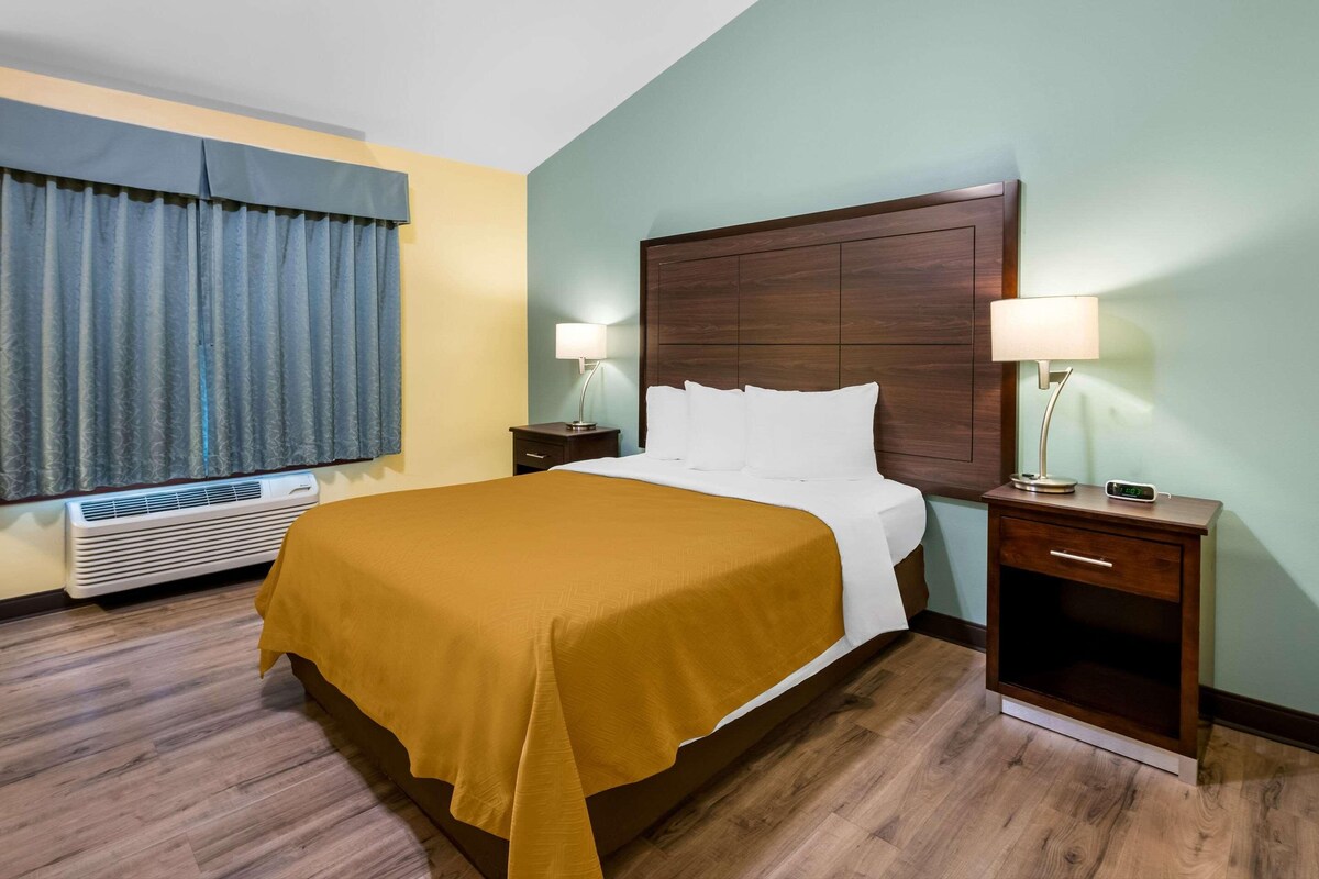Habitación de hotel con una cama grande, un cabecero de madera, dos mesitas de noche con lámparas, un calentador y una ventana con cortinas.