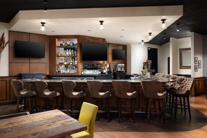 Un espace bar moderne avec un comptoir en bois, de nombreux tabourets et un grand téléviseur à écran plat fixé au mur.