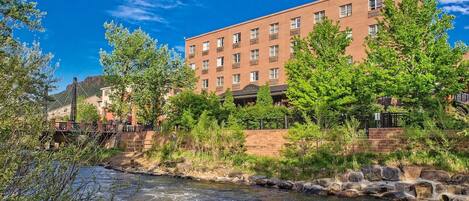A multi-story hotel with a brick facade, a river in the foreground, and a clear blue sky.