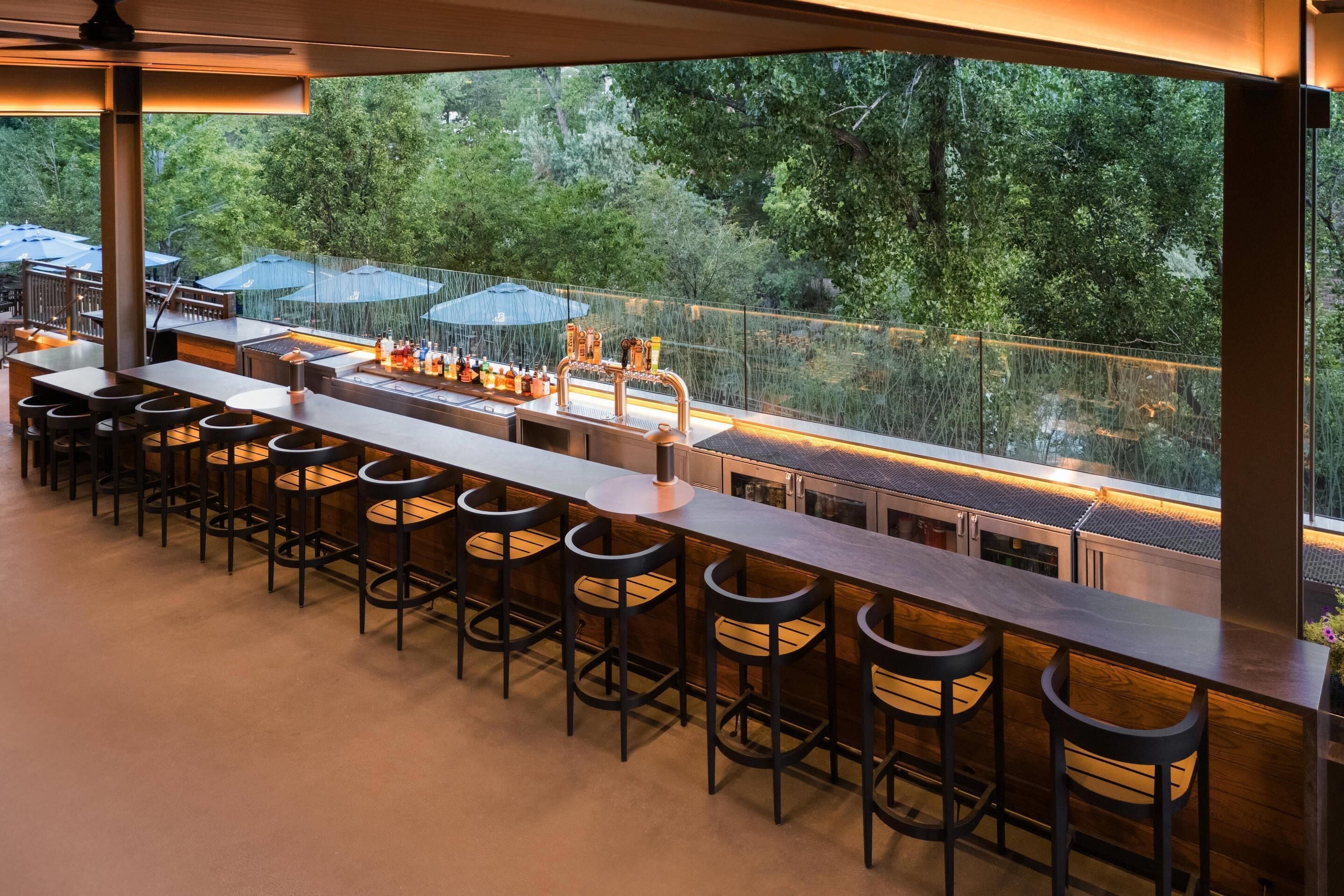 An outdoor bar area with multiple seating options and a view of the surrounding greenery.