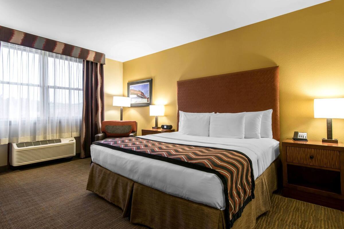 A hotel room with a large bed, two bedside tables, a wall-mounted TV, and a window with curtains.