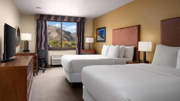 Habitación de hotel con dos camas, un escritorio, un televisor y ventana con vista a la montaña.