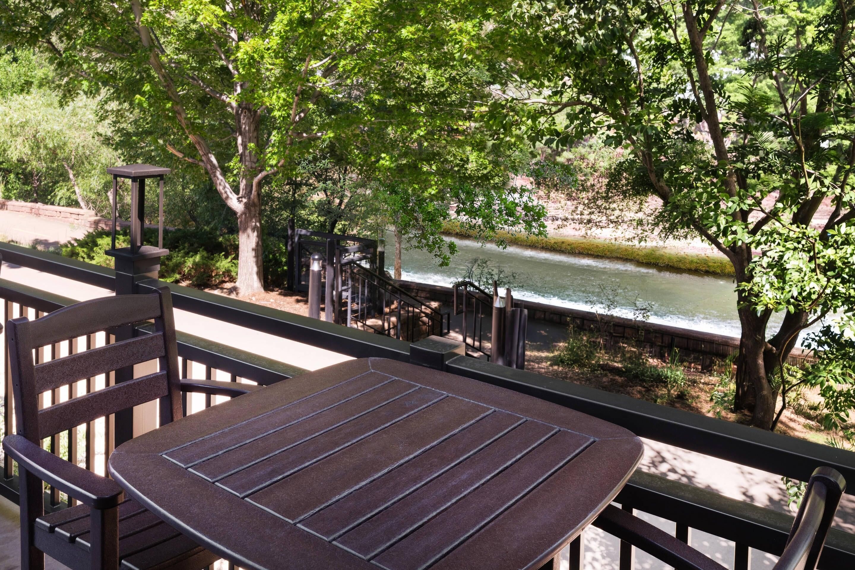 A table and chairs on a balcony with a view of a river and trees.