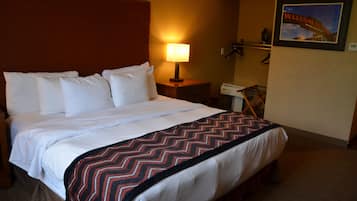 A hotel room with a large bed, a nightstand with a lamp, a desk with a telephone, and a welcome sign on the wall.