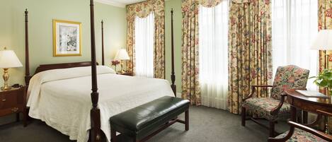 A four-poster bed with a bench, floral curtains, and a chair with a floral pattern.