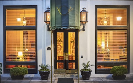 A hotel entrance with a dark-colored door, two potted plants on either side, and a green awning above.