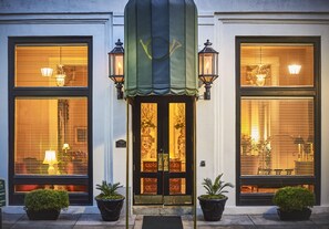 A hotel entrance with a dark-colored door, two potted plants on either side, and a green awning above. - Planters Inn on Reynolds Square (Savannah)