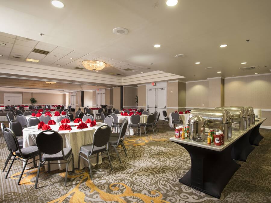 A banquet hall with round tables, chairs, and a buffet area.