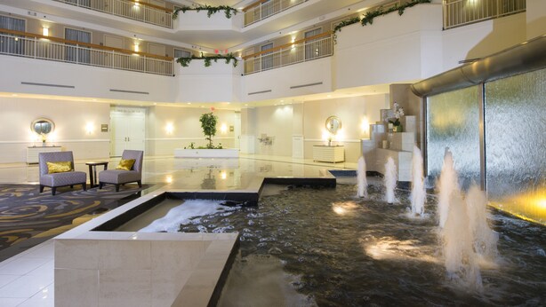 A multi-level hotel lobby with a central water feature, seating areas, and a reception desk.