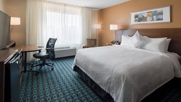 A hotel room with a bed, a desk, a chair, a lamp, and a window with curtains.