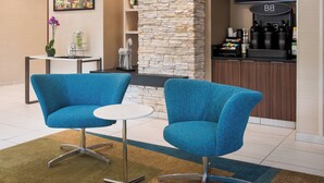 A modern hotel lobby with two blue armchairs, a stone accent wall, a coffee station, and a flat-screen TV.