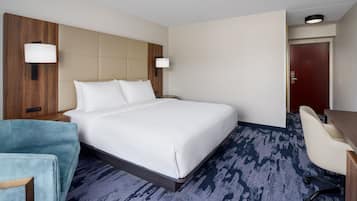 A hotel room with a large bed, a desk, a chair, and a wooden headboard.