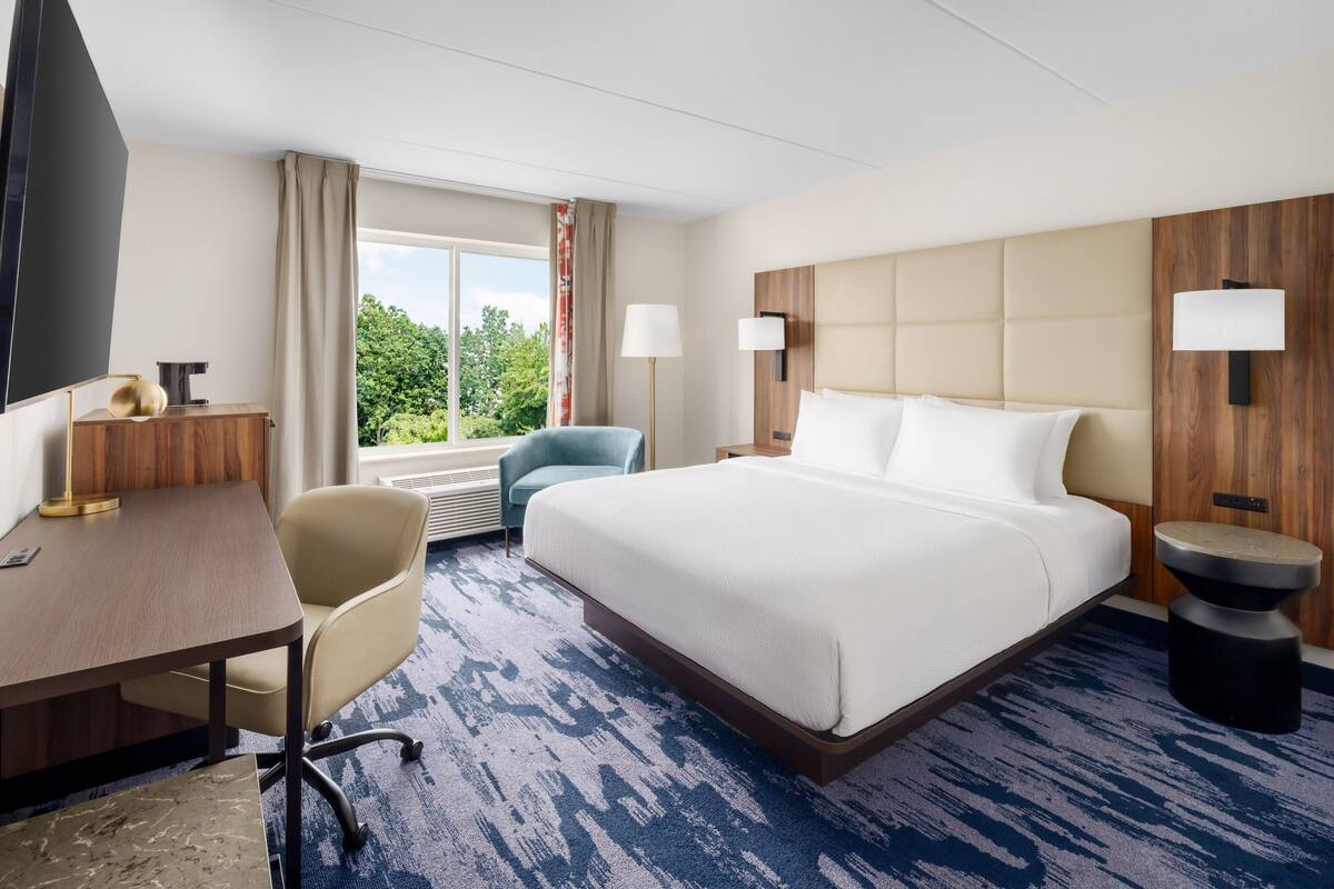 Une chambre d’hôtel avec un grand lit, un bureau, une chaise et un téléviseur.