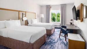 Habitación de hotel con dos camas, un escritorio, una silla, un televisor y una ventana con cortinas.