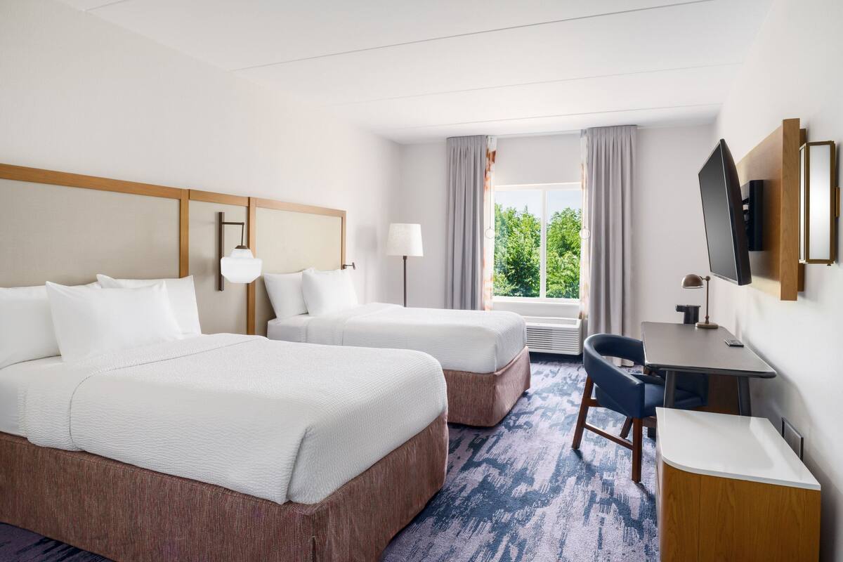 Une chambre d’hôtel avec deux lits, un bureau, une chaise, une télévision et une fenêtre avec des rideaux.