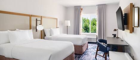 A hotel room with two beds, a desk, a chair, a TV, and a window with curtains.