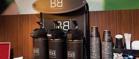 Una estación de café con una máquina de café de marca, varios dispensadores de café y una variedad de vasos y recipientes desechables.