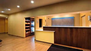 A hotel reception area with a wooden reception desk, a black mat at the entrance, and a vending machine with snacks. - Fairfield Inn by Marriott Huntsville (Huntsville)