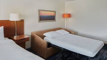 Quarto de hotel com uma cama de solteiro, mesa de cabeceira com abajur, pintura pendurada na parede e luminária para leitura individual.