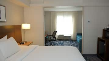 A hotel room with a bed, a desk, a chair, a lamp, and a television.