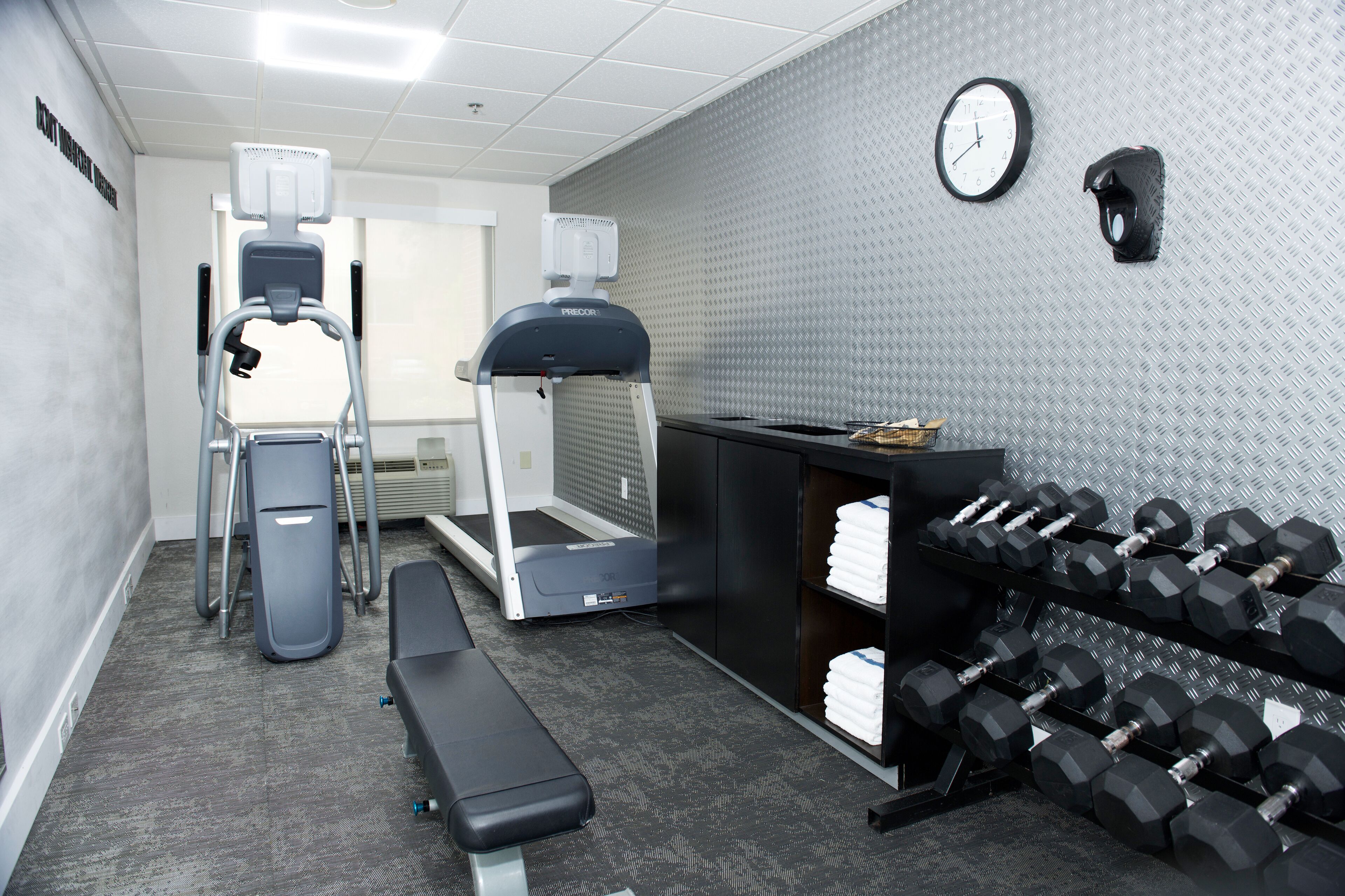 A gym with treadmills, a bench, and a rack of dumbbells.