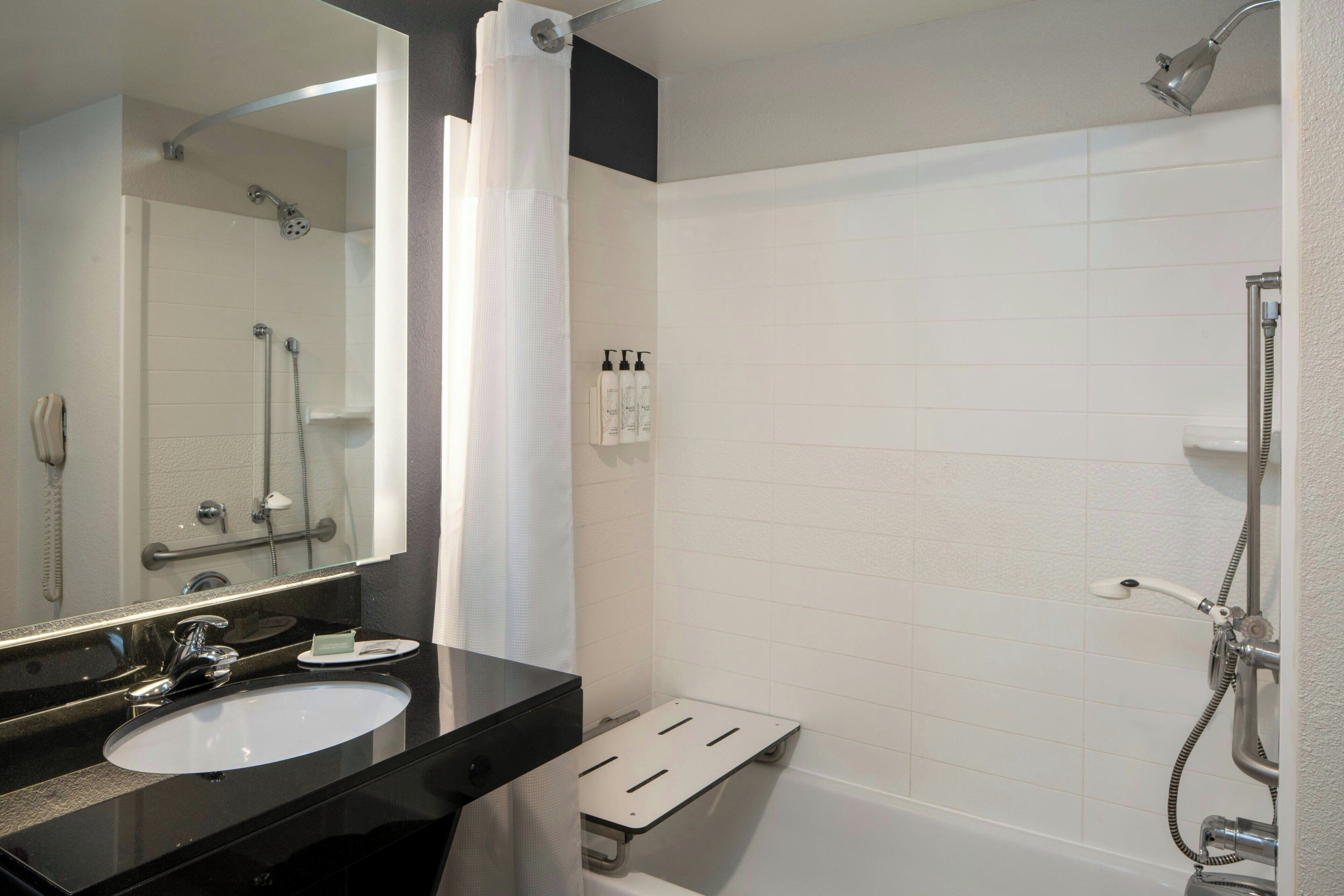 A modern bathroom with a black sink, a large mirror, a shower with a handheld showerhead, and a white tiled wall.
