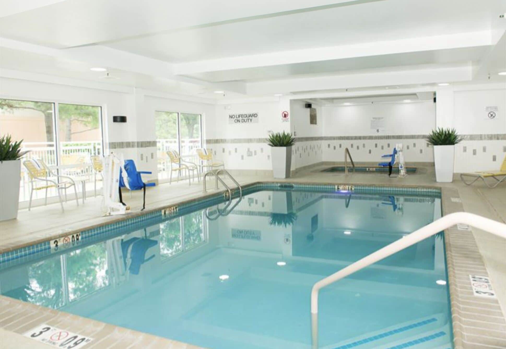 Piscina interna con acqua cristallina, cartello con bagnino in servizio e sedie a sdraio nella zona piscina.