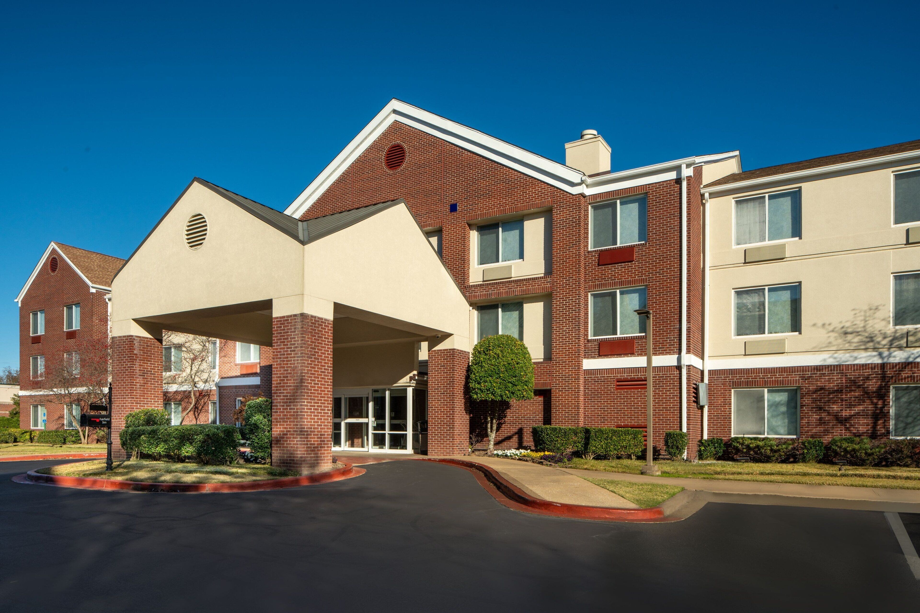 A multi-story hotel with a central entrance, brick facade, and a landscaped front yard.