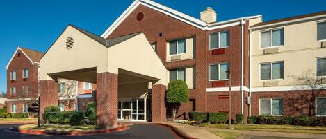A multi-story hotel with a central entrance, brick facade, and a landscaped front yard.