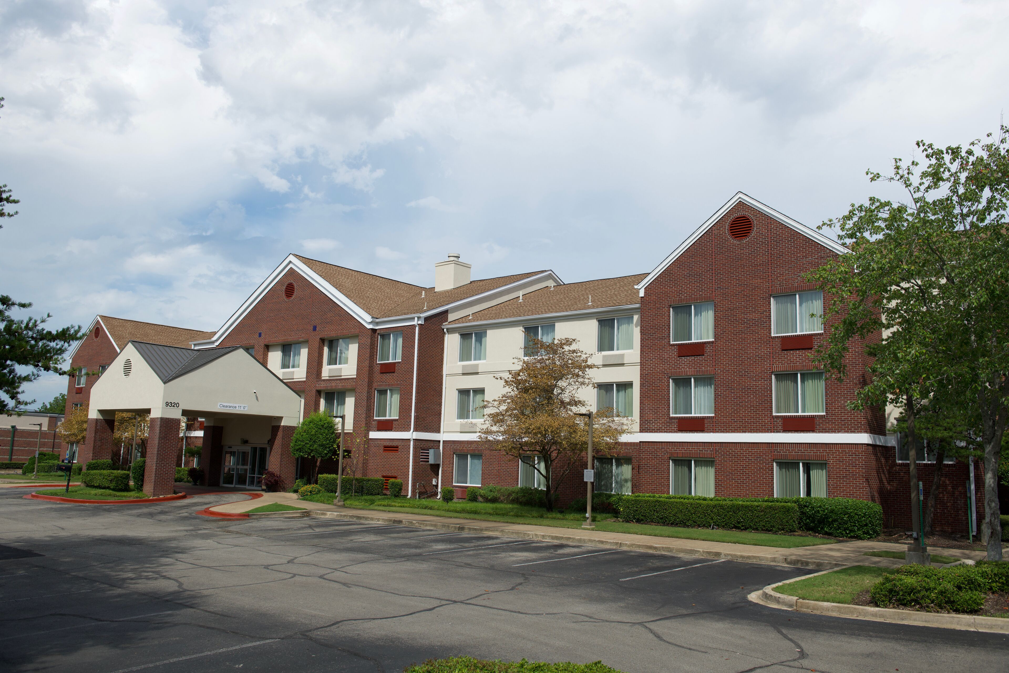 A multi-story hotel with a brick facade, a covered entrance, and a parking lot.